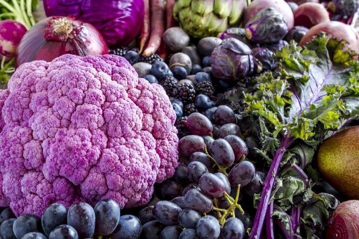 Arrangement van blauwe en paarse vruchten en groenten waaronder druiven, pruimen, bessen, rode uien en rode kool