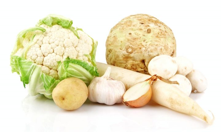 Een arrangement van bruine en witte groenten, waaronder aardappel, bloemkool, ui, knoflook, selderij, champignons en wortels.